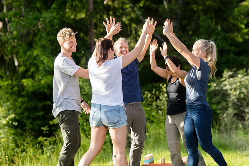 Fem glade kollegaer jubler og giver high-fives til udendørs teambuilding på Sjælland.